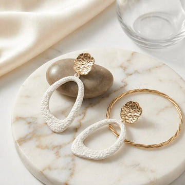 Pair of gold and white hoop earrings on a marble surface.