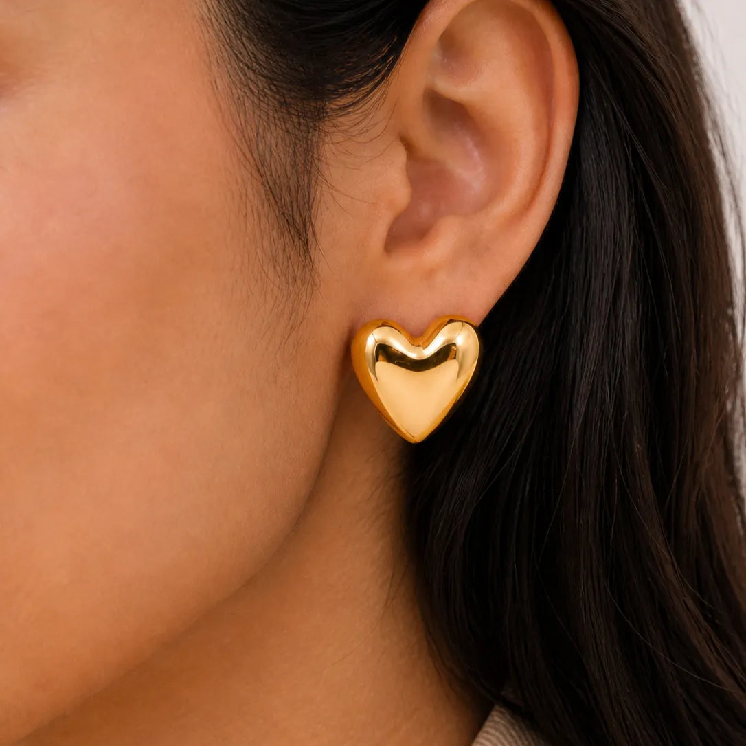 Gold heart-shaped earring worn by a person with dark hair.