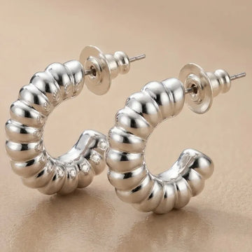 Silver hoop earrings with a ribbed texture on a beige background