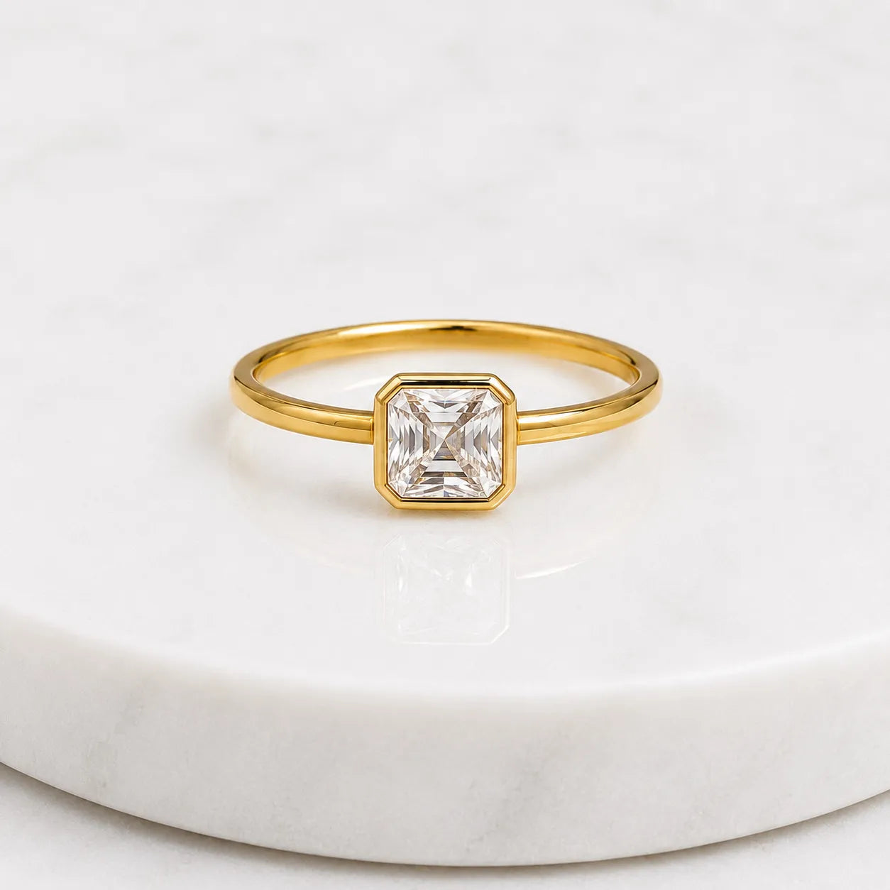 Gold ring with a square-cut diamond on a white marble surface