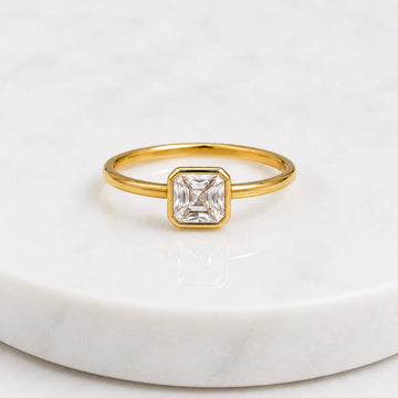 Gold ring with a square-cut diamond on a white marble surface