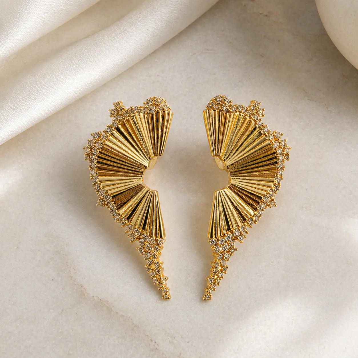 Gold earrings with fan-like design on a beige fabric background