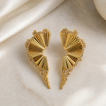 Gold earrings with fan-like design on a beige fabric background