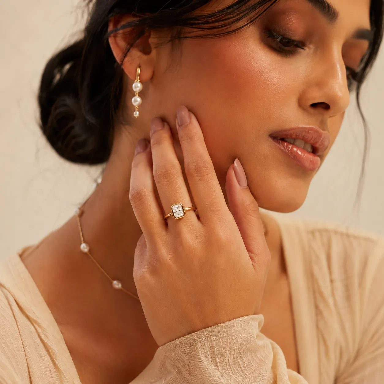 Woman wearing pearl earrings and a ring, with a neutral background