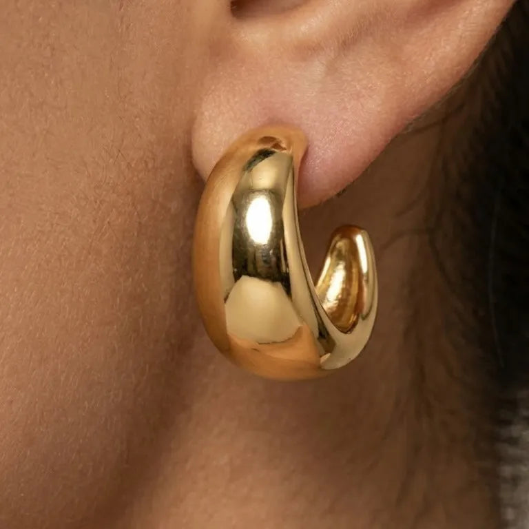 Gold hoop earring worn on an ear with a neutral background