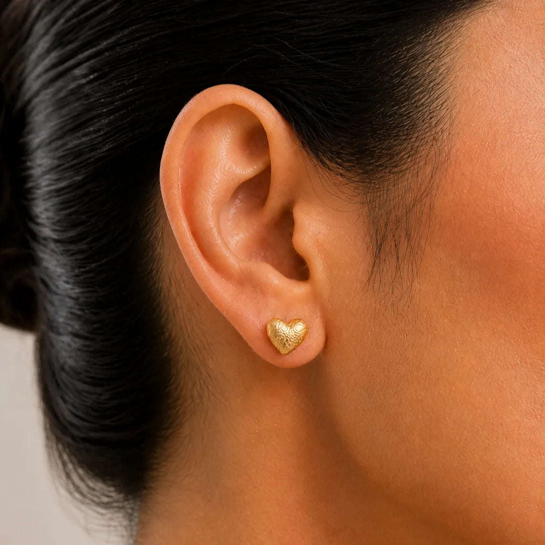 Close-up of an ear wearing a gold heart-shaped earring with a blurred background