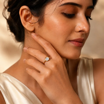 Woman wearing a gold ring with a diamond, touching her neck against a warm-toned background