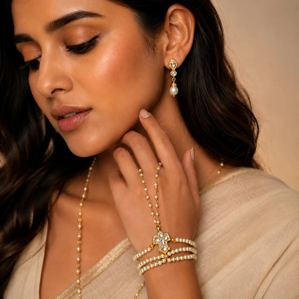 Woman wearing gold jewelry including earrings, necklace, and bracelets against a beige background