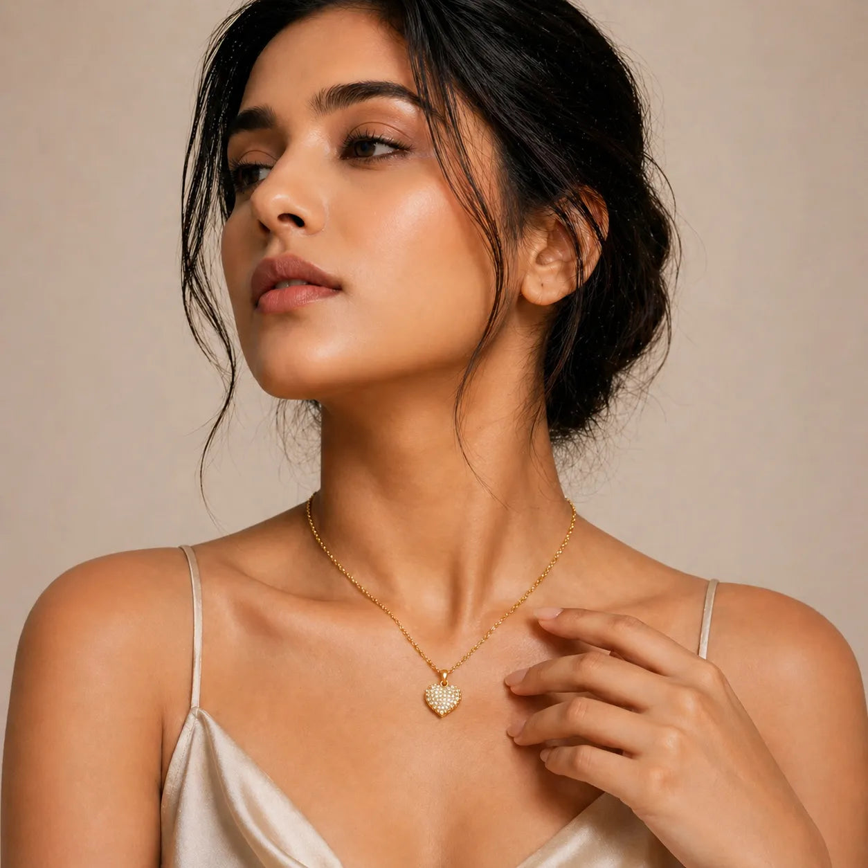 Woman wearing a gold necklace with a heart pendant against a beige background