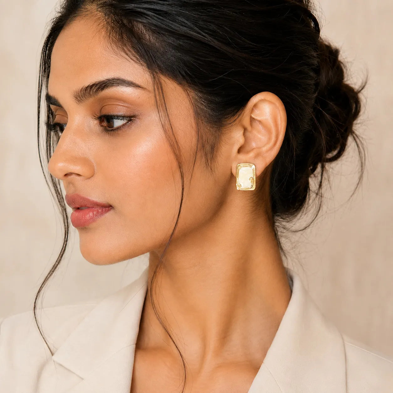 Close-up of a woman wearing gold earrings with a neutral background
