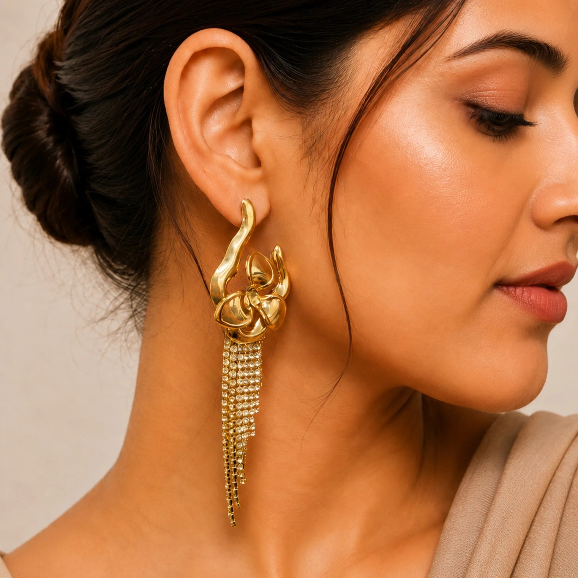 Close-up of a woman wearing a gold earring with tassels against a neutral background