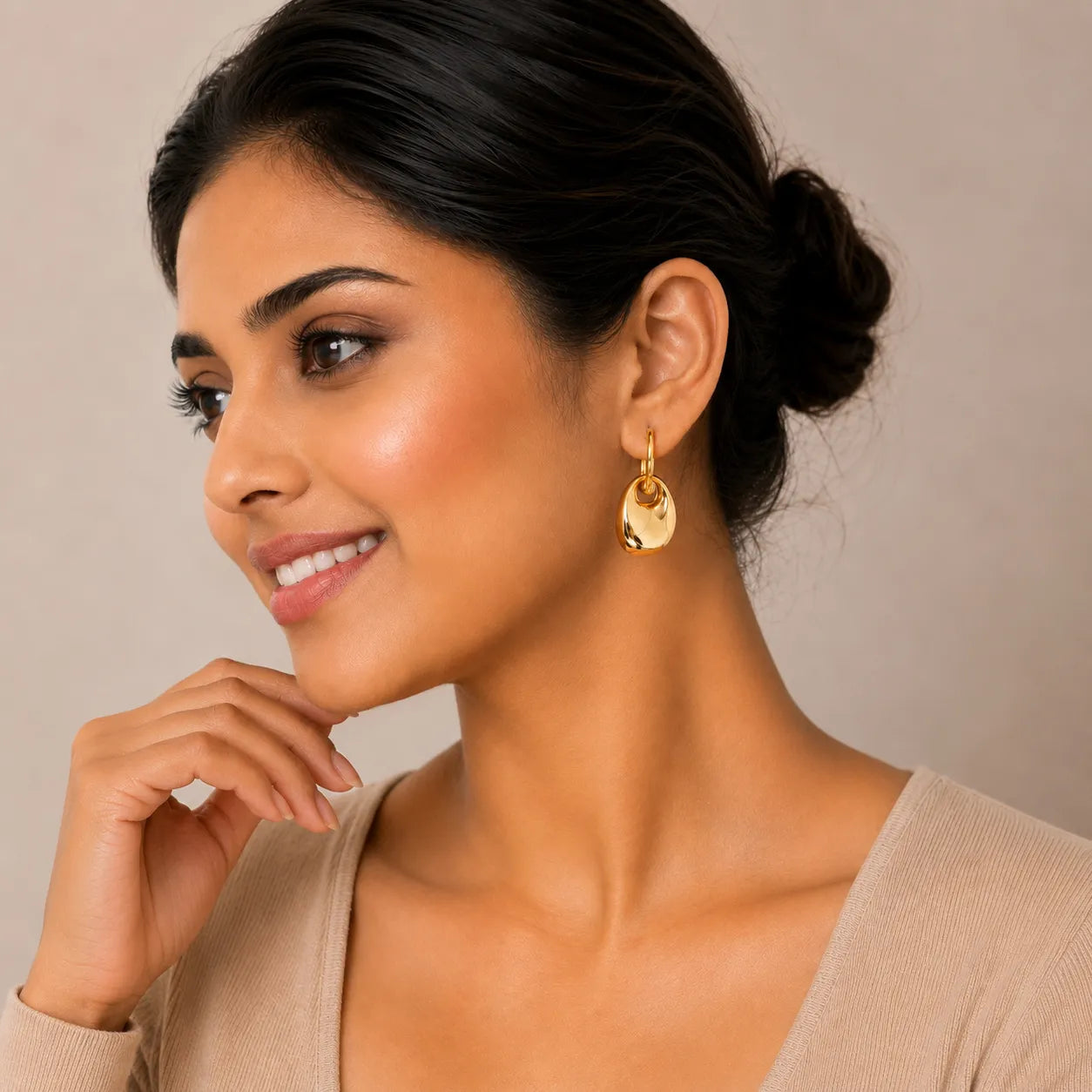 Woman wearing gold earrings against a neutral background