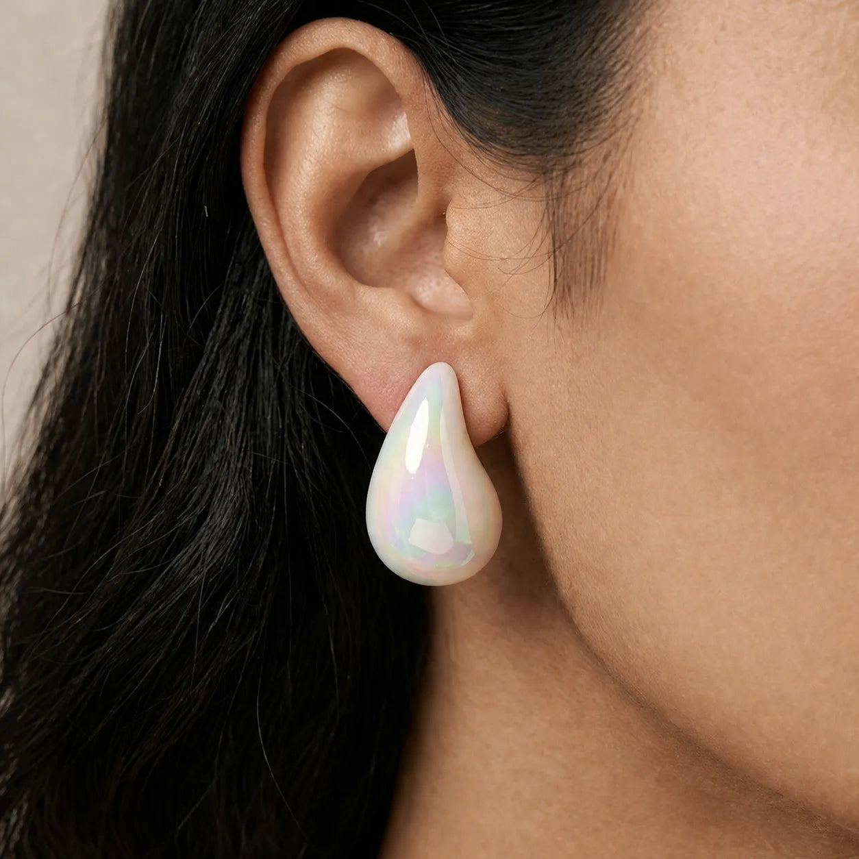 Close-up of a person wearing a teardrop-shaped iridescent earring.