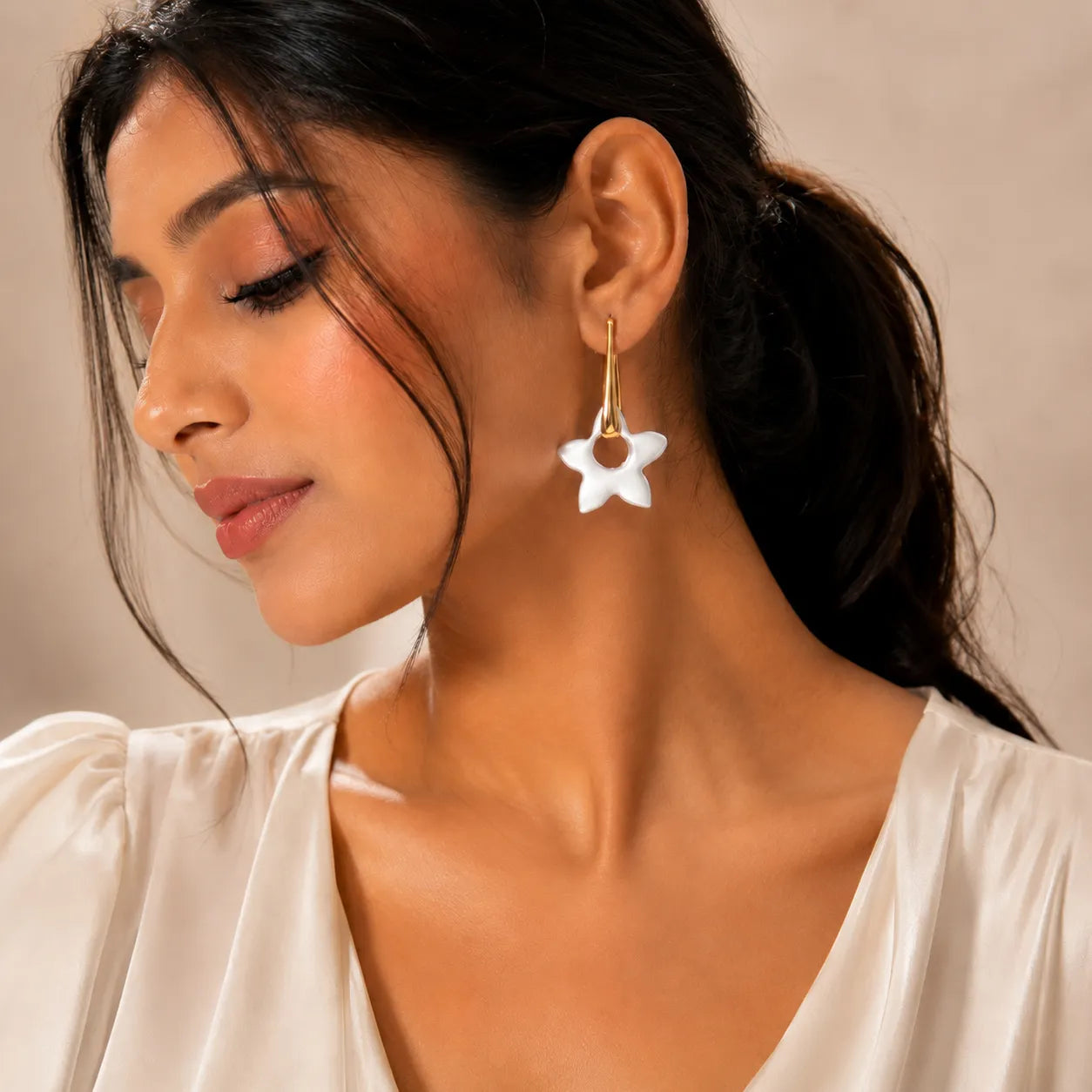 Close-up of a woman wearing a white flower earring against a neutral background