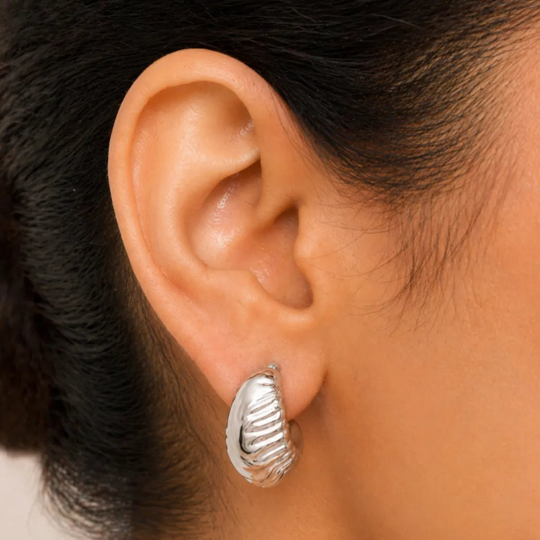 Close-up of an ear wearing a silver earring with dark hair.