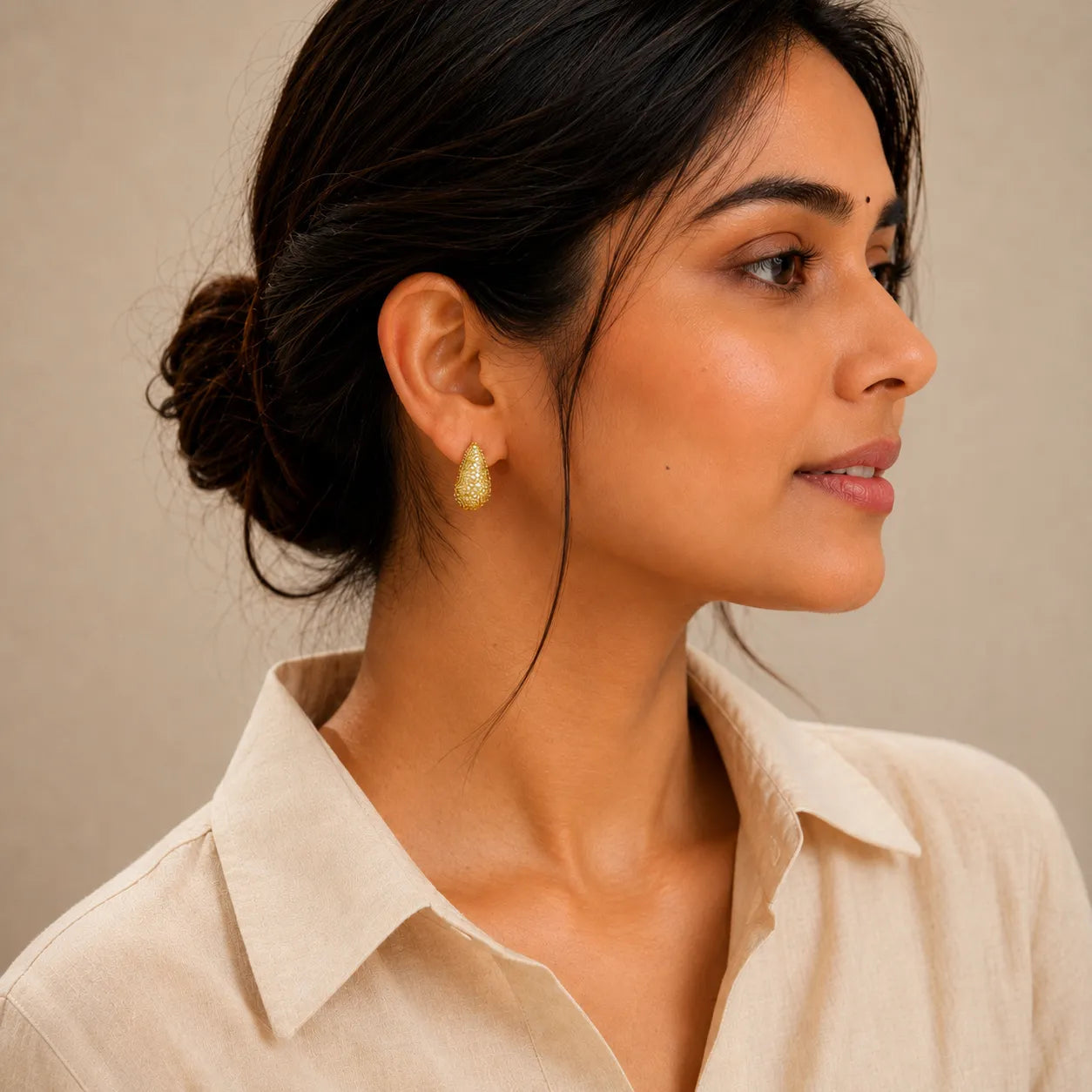 Woman wearing gold earrings with a neutral background