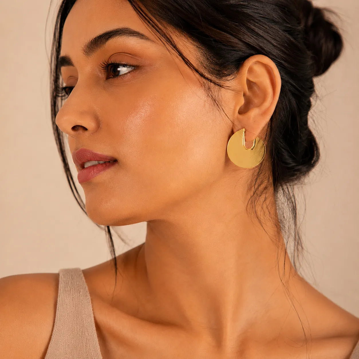 Woman wearing gold earrings against a beige background