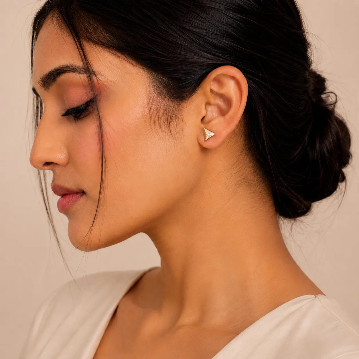 Close-up of a woman wearing a triangle-shaped earring against a neutral background