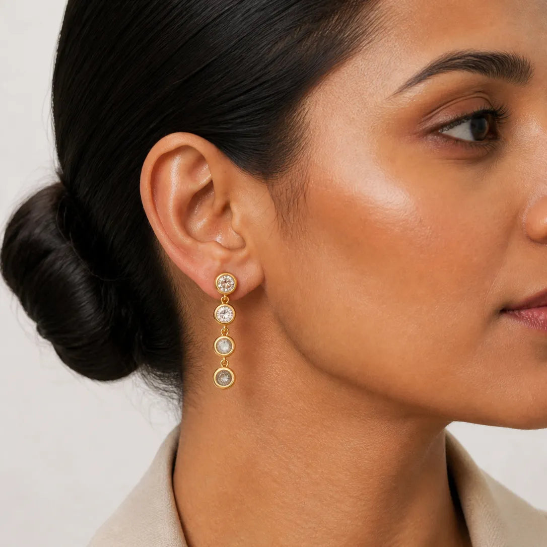 Close-up of a woman wearing gold earrings with clear stones on a neutral background
