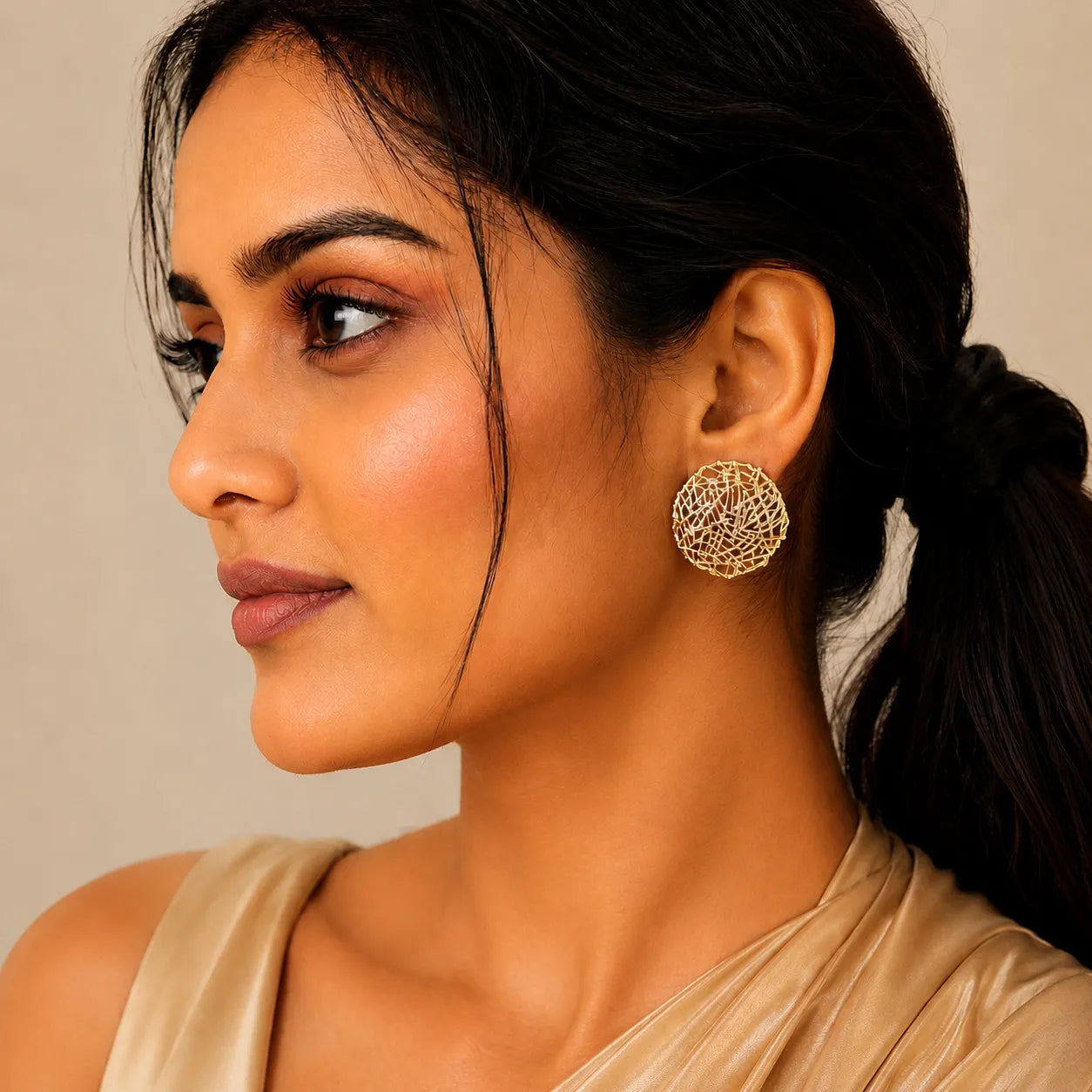 Woman wearing gold earrings with a neutral background