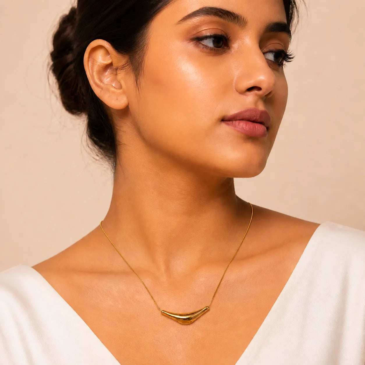 Woman wearing a gold necklace against a beige background
