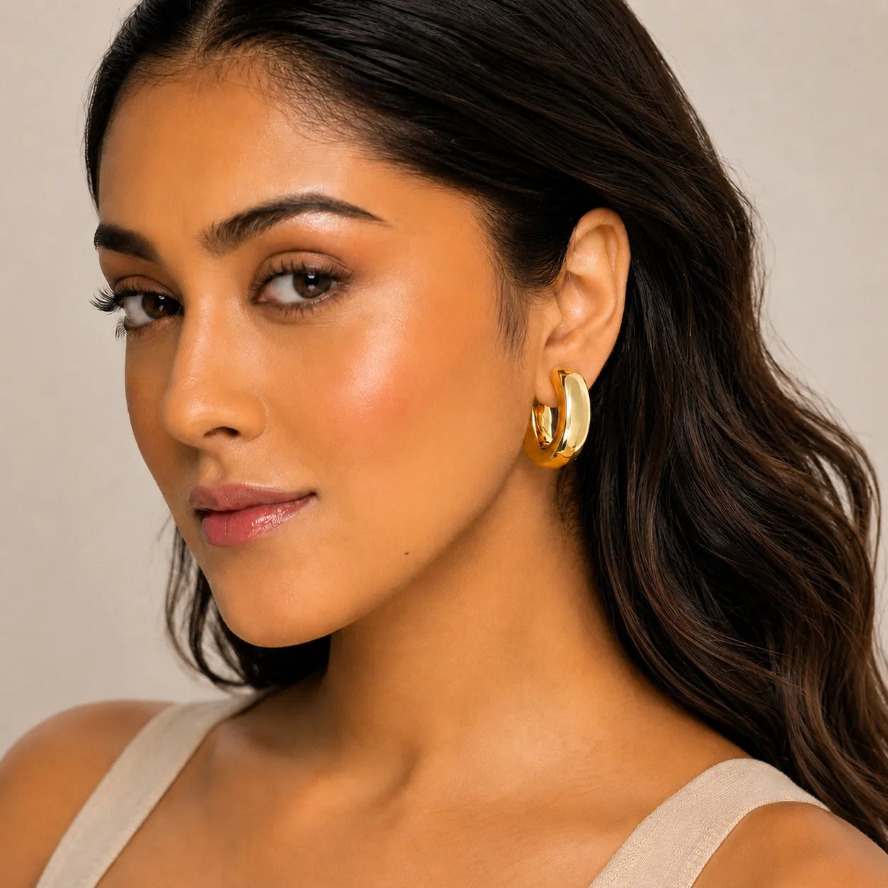 Woman wearing gold hoop earrings with a neutral background