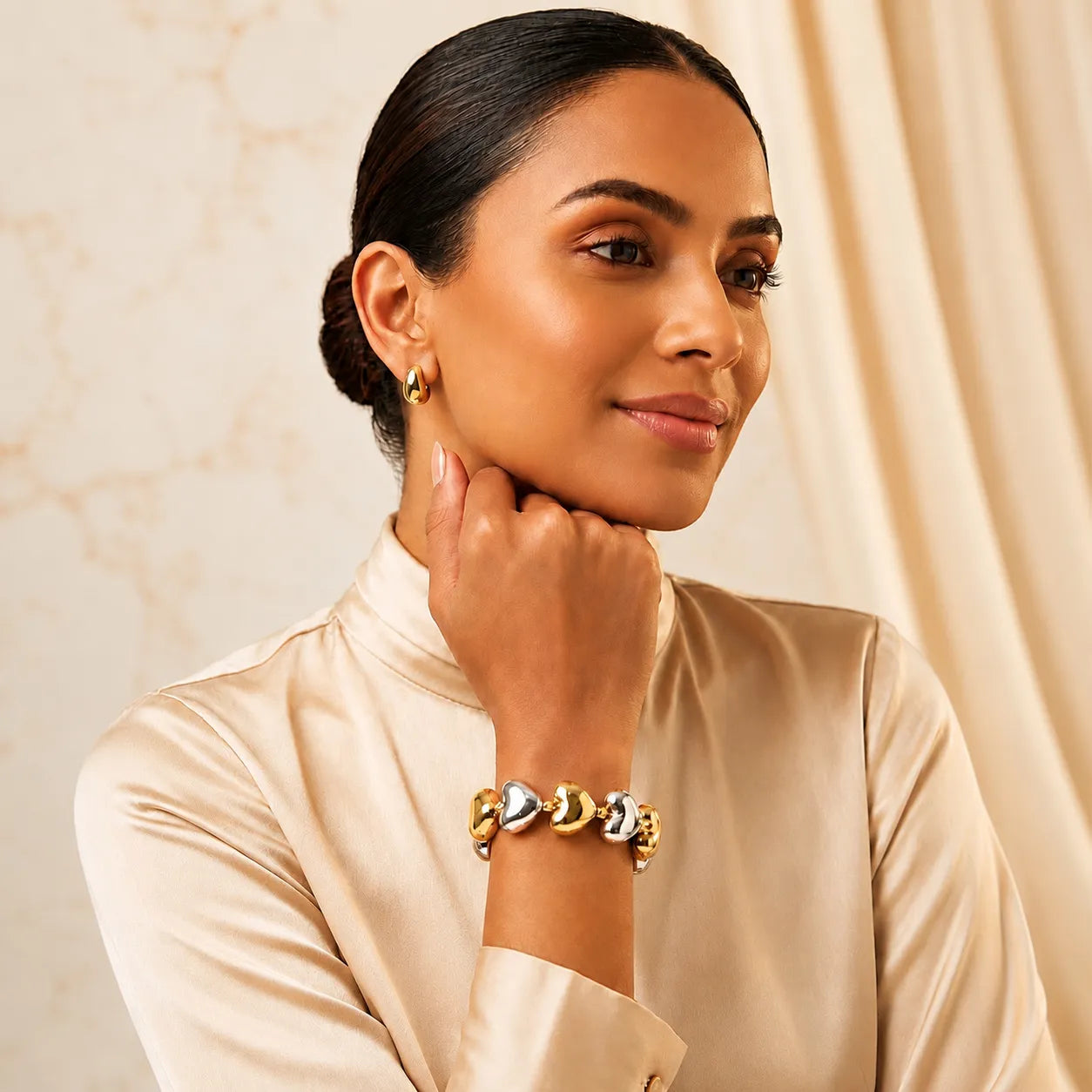 Woman wearing gold jewelry against a beige background
