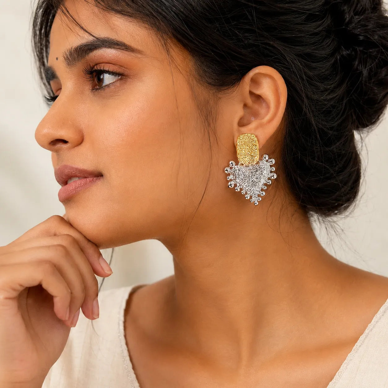 Close-up of a woman wearing gold and silver earrings with a neutral background