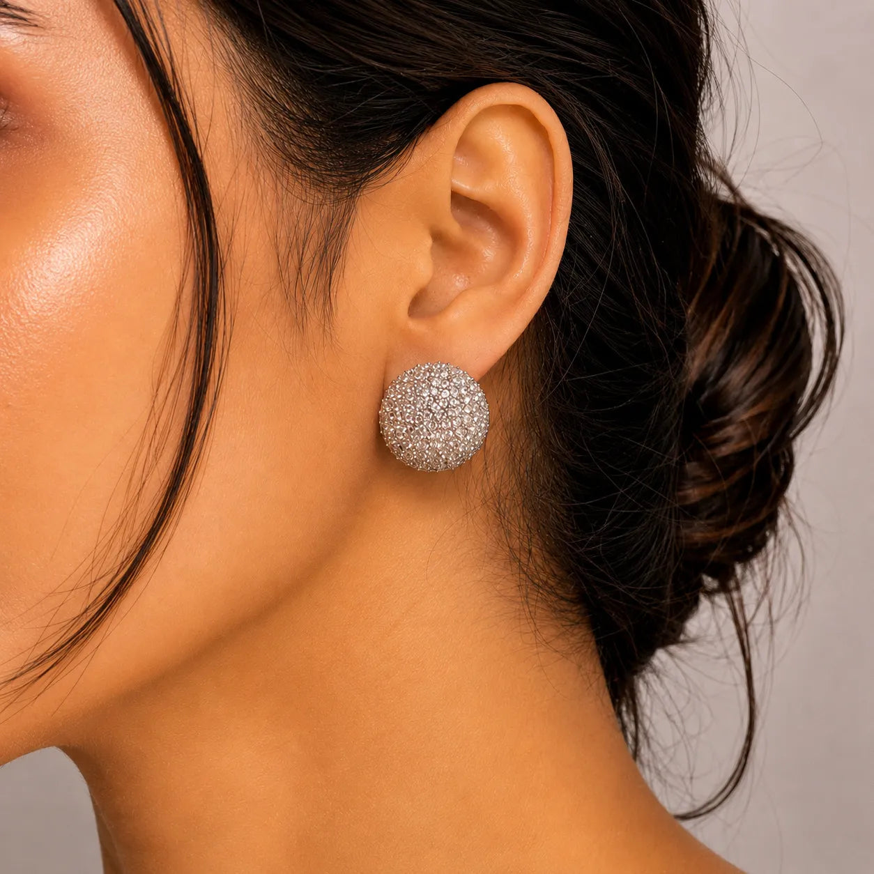 Close-up of a person wearing a sparkling silver earring against a neutral background
