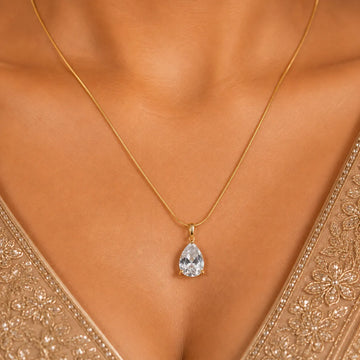 Gold necklace with a teardrop-shaped pendant on a model wearing an embroidered garment.