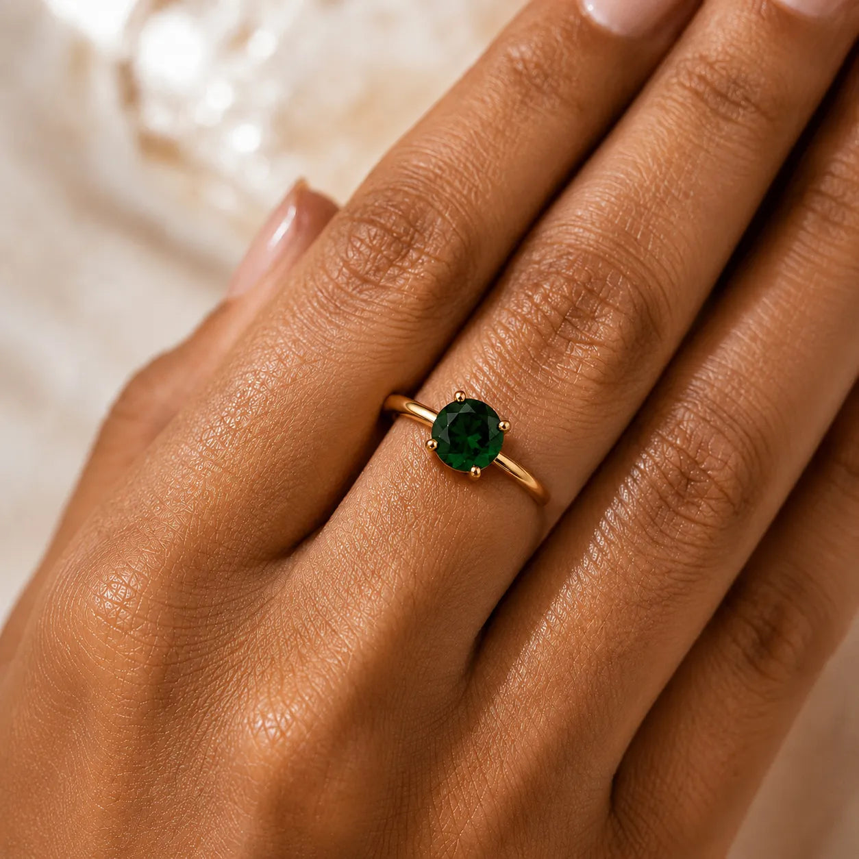 Gold ring with a green gemstone on a hand against a neutral background