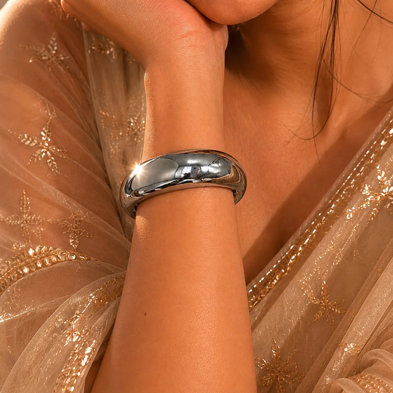 Silver bracelet on a wrist with a sheer fabric background