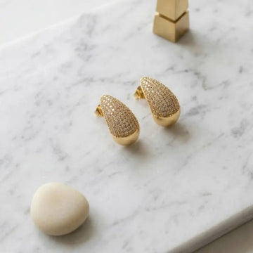 Gold teardrop-shaped earrings on a marble surface