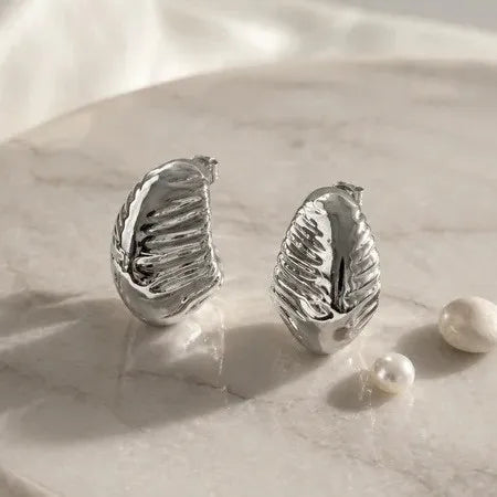 Silver leaf-shaped earrings on a marble surface with pearls.