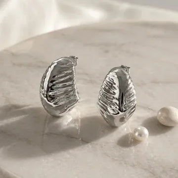 Silver leaf-shaped earrings on a marble surface with pearls.