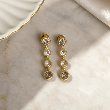 Gold earrings with clear stones on a marble surface