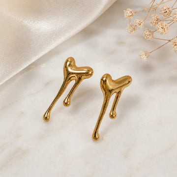 Gold heart-shaped earrings on a light beige background with dried flowers.