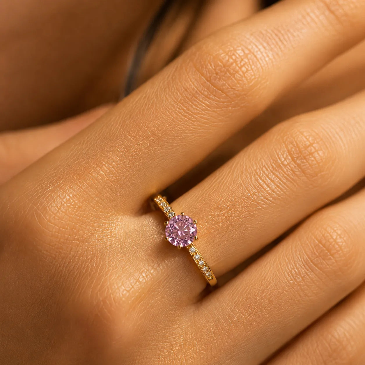 Close-up of a hand wearing a pink gemstone ring with gold band.