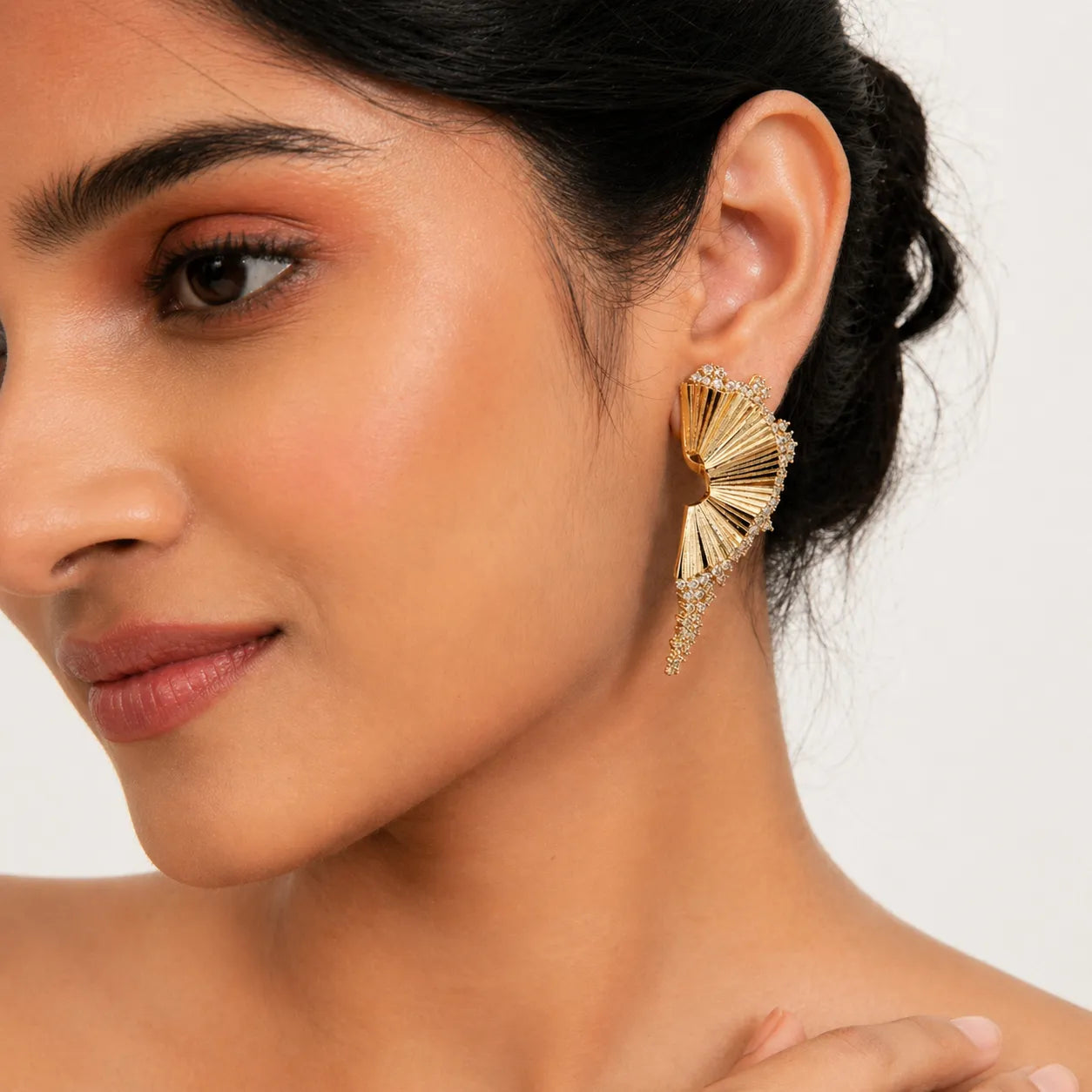 Close-up of a woman wearing a gold earring with a white background