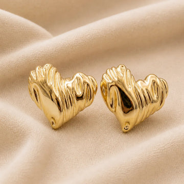 Gold heart-shaped earrings on a beige fabric background