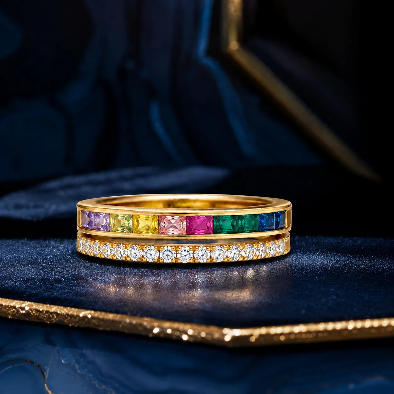 Two gold rings with colorful gemstones and diamonds on a dark blue background