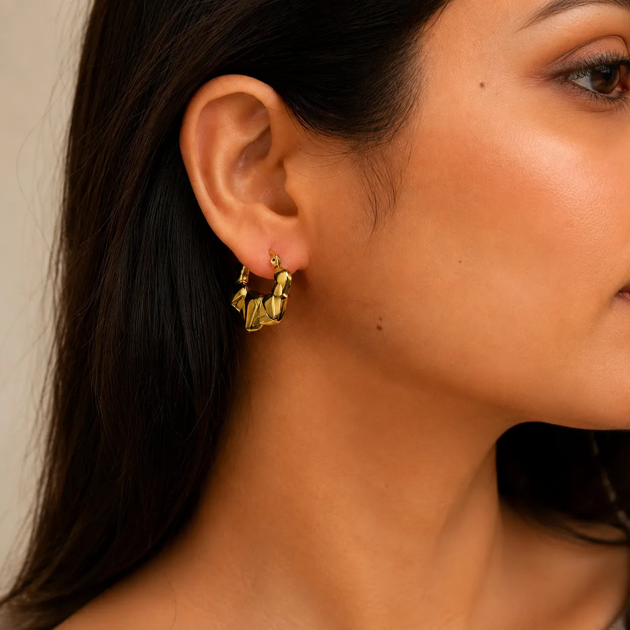 Close-up of a person wearing a gold earring with a neutral background