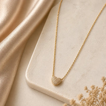 Gold necklace with a heart-shaped pendant on a beige fabric background