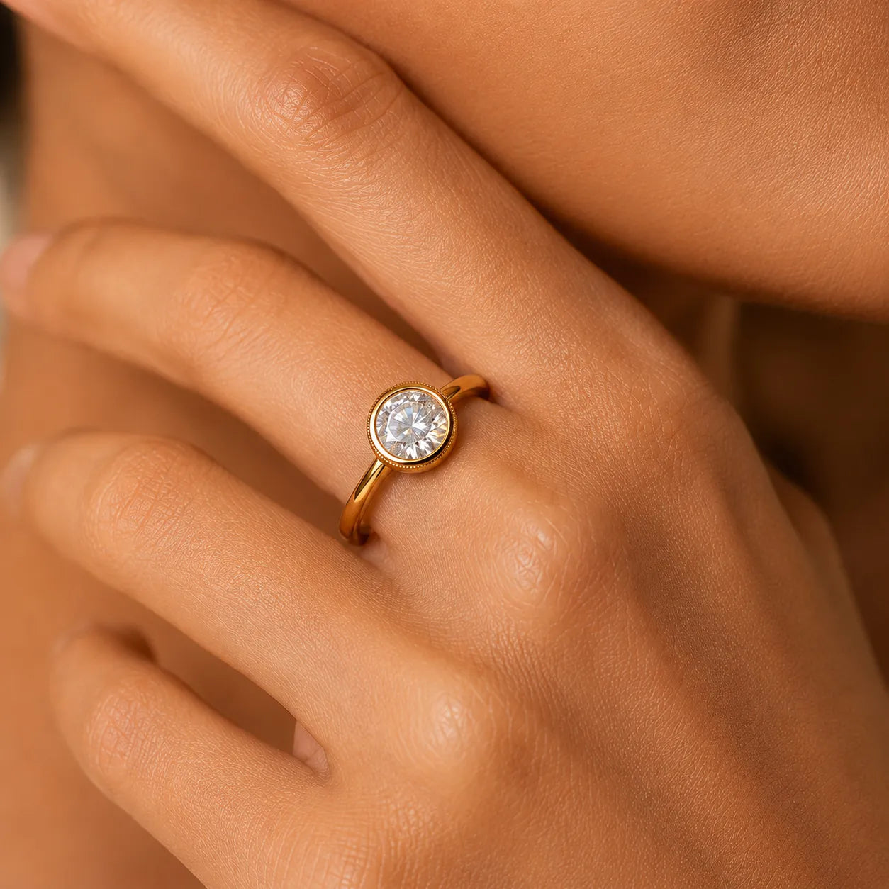 Gold ring with a diamond on a person's finger against a neutral background