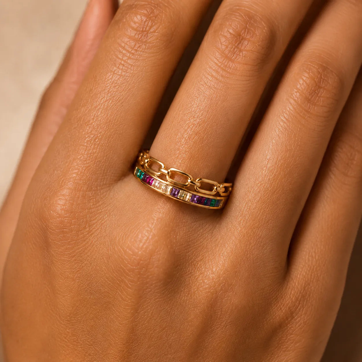 Gold ring with colorful gemstones on a hand against a neutral background