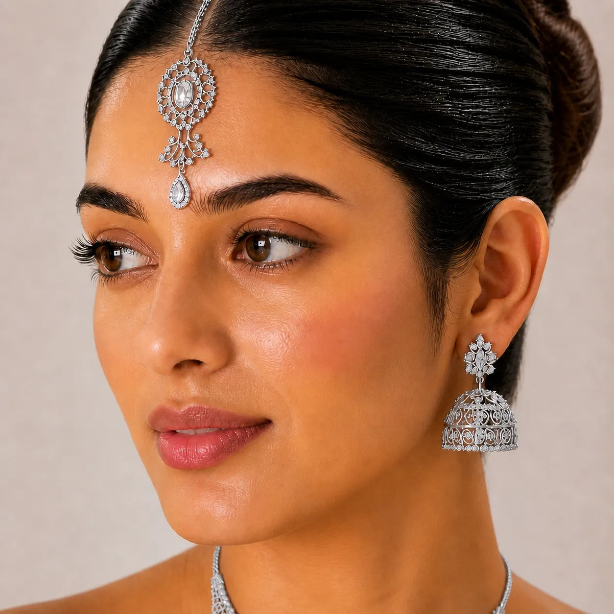 Close-up of a woman wearing silver jewelry including earrings and a necklace on a neutral background