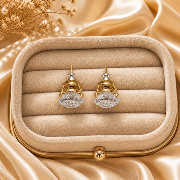 Gold earrings with clear gemstones in a beige jewelry box on a beige fabric background
