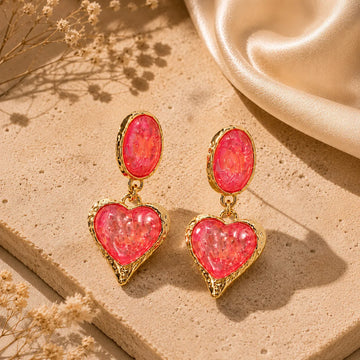 Heart-shaped earrings with pink stones and gold frames on a beige surface.