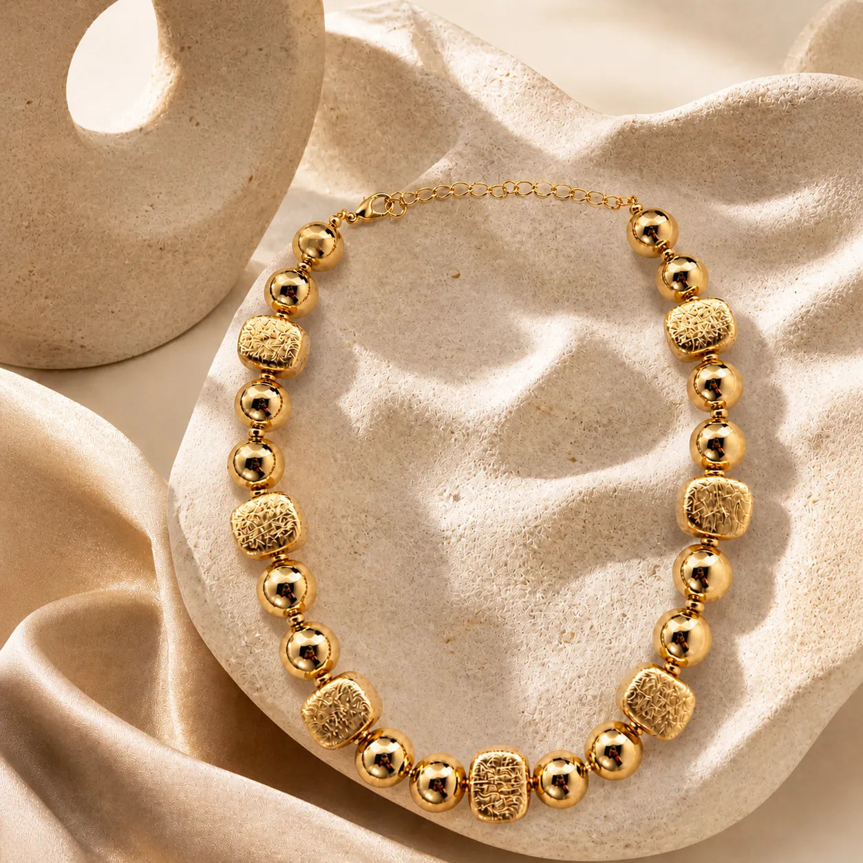 Gold necklace with textured beads on a beige fabric background