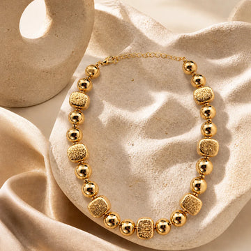 Gold necklace with textured beads on a beige fabric background
